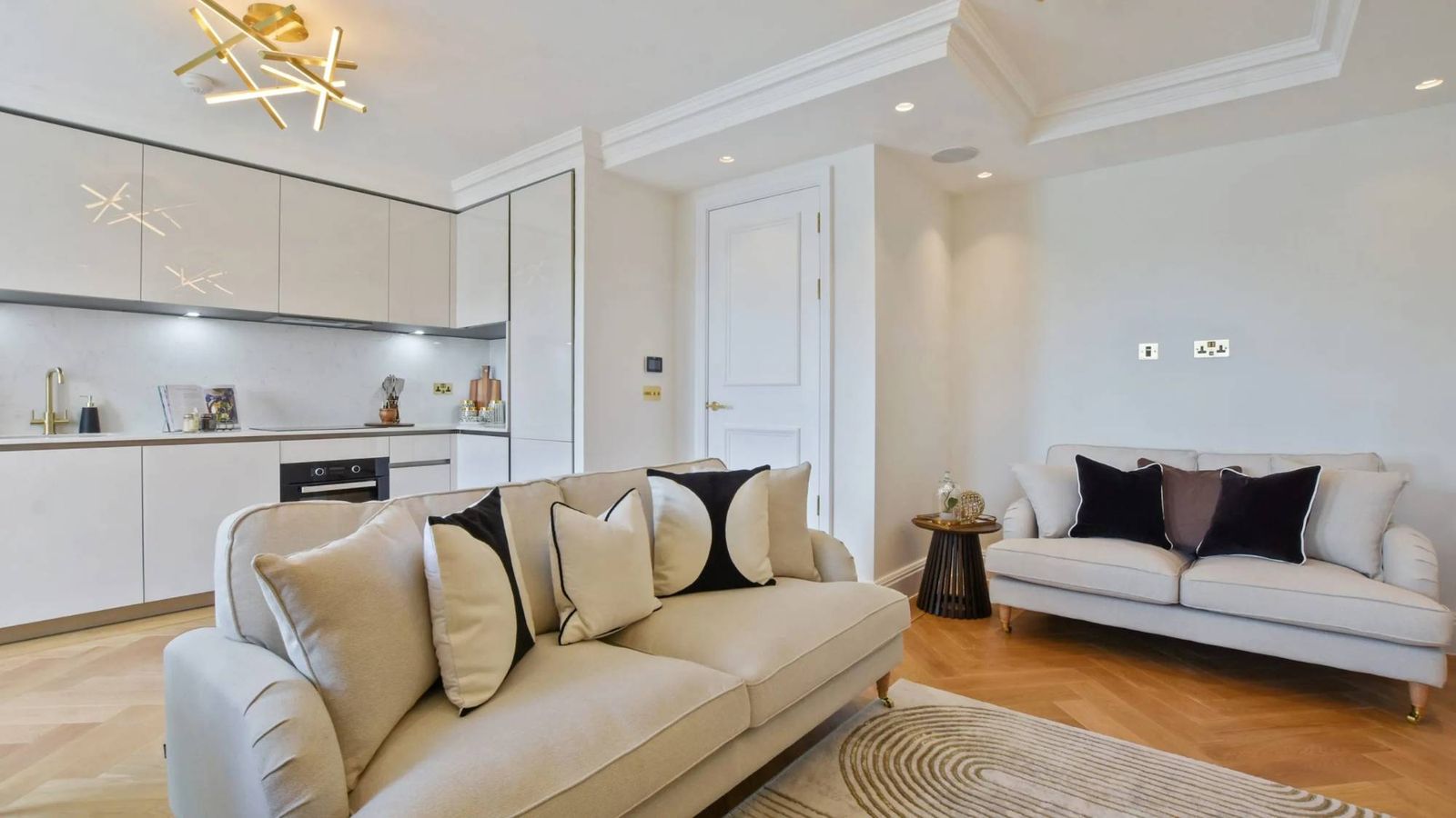 Staged open-plan living room and kitchen with cream sofas, herringbone floor and brass lighting
