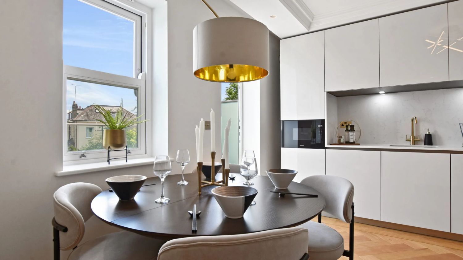 Staged dining area set for four beside a sash window, with a gold-lined pendant shade