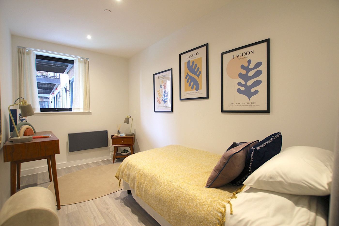 Staged second bedroom with a yellow throw, mid-century desk and framed prints