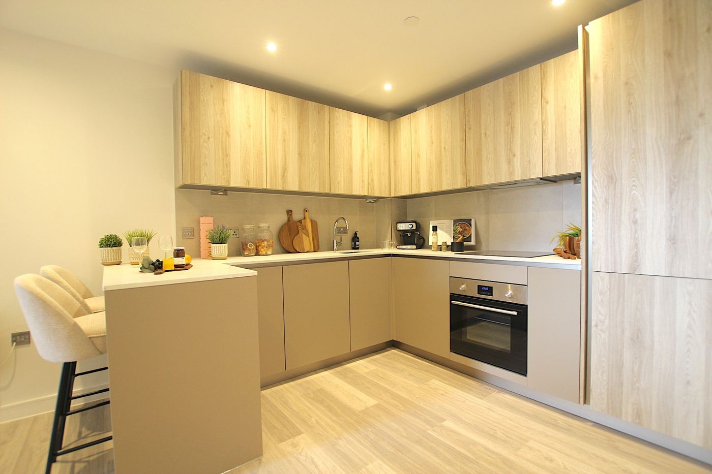 Staged kitchen with oak-effect wall units, taupe base units and a breakfast bar with two stools