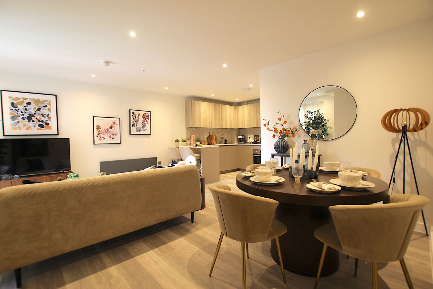 Staged open-plan living and dining room with a round dark-wood table set for four, velvet chairs and a corduroy sofa