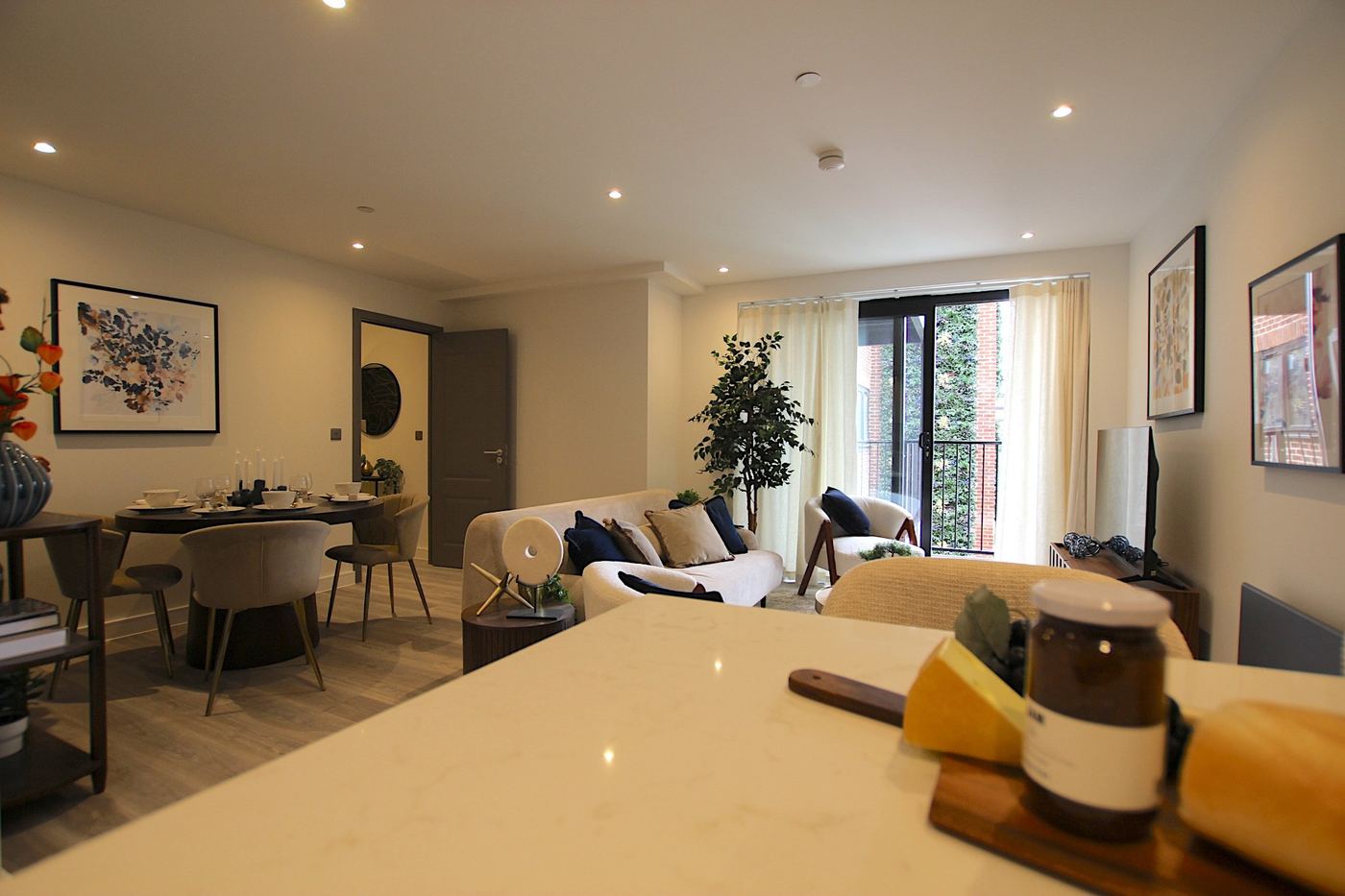 View across a staged living room from the kitchen worktop towards the balcony doors